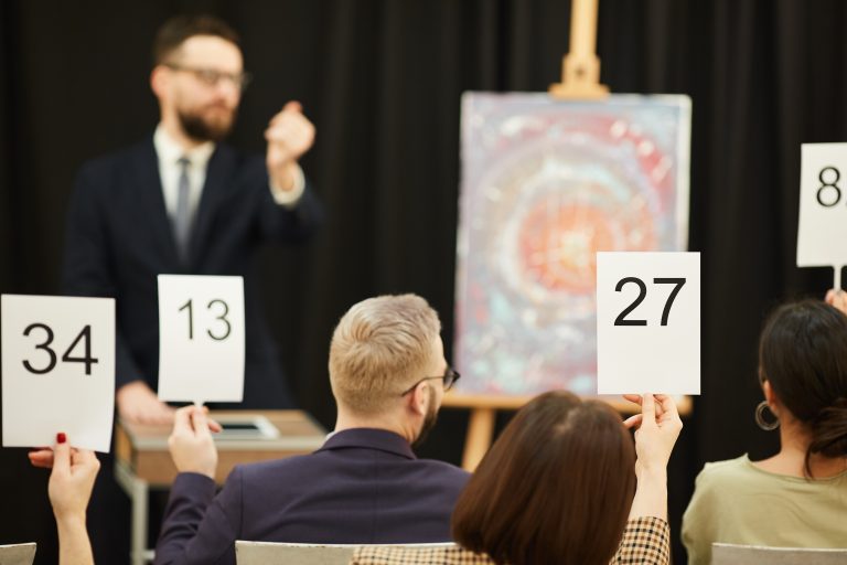 Rear view of group of business people with signs buying a painting during the auction