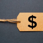 A brown cardboard price tag with a twine string and a black dollar sign symbol, influenced by the Link Tax Law, set against a dark gray background.