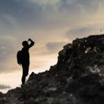 Man getting ready to climb up mountain looking up at the challenge before him planning path.